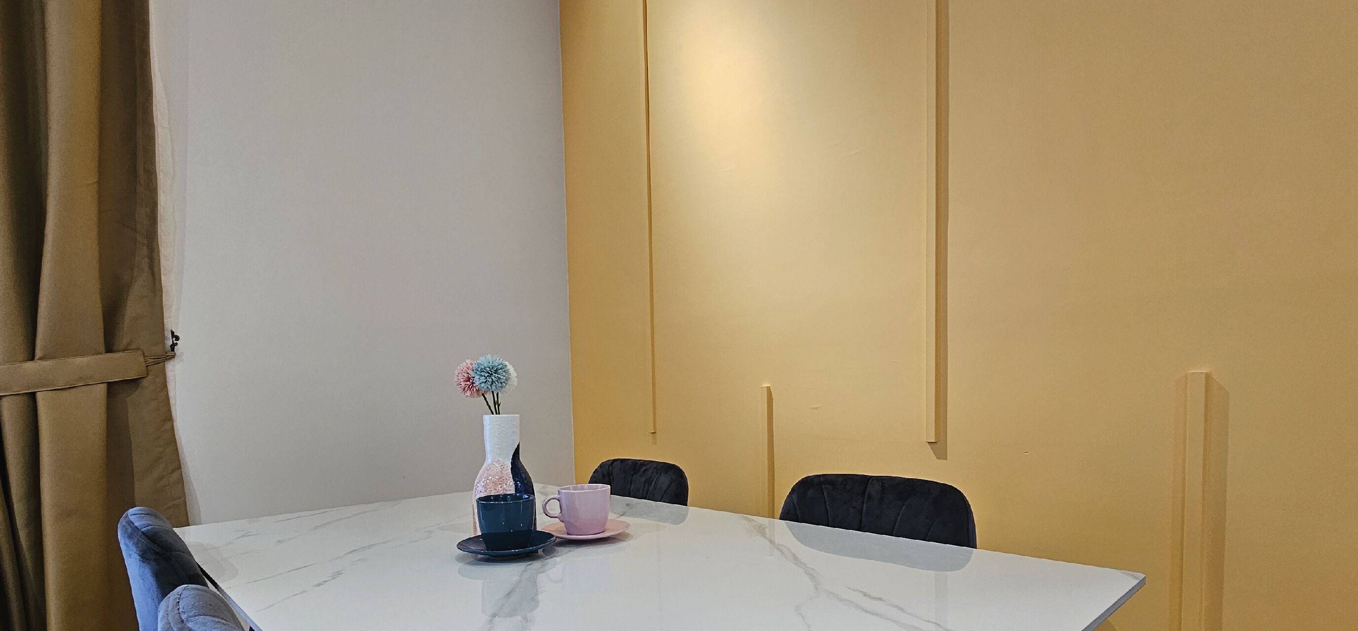 A conference room with a white table, two chairs, a vase with flowers, and a pink mug.