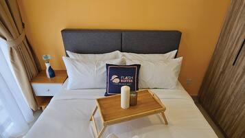 Una habitación de hotel con una cama, una mesita de noche, una mesilla auxiliar, una bandeja de madera con una vela y un cojín con un logotipo.