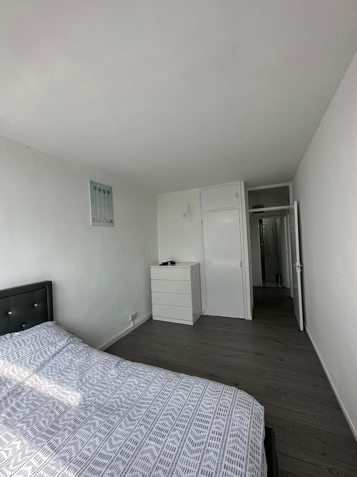 A bedroom with a bed, a dresser, and a wardrobe. There is a door leading to another room.