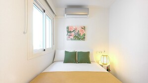 A neatly arranged bedroom with a bed, a window, an air conditioner, a wall-mounted lamp, and a floral painting. - 2 bedroom, city and sea (Fuengirola)