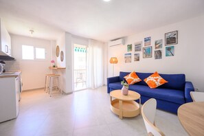 Una sala de estar moderna con un sofá azul, una mesa de centro redonda y una zona de comedor con una mesa y sillas de madera.