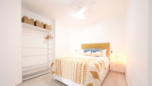 Une chambre à coucher comprenant un lit, un ventilateur de plafond, une table de chevet et des étagères de rangement.