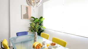 Un comedor moderno con una mesa de vidrio, sillas amarillas, un jarrón con flores y una planta.