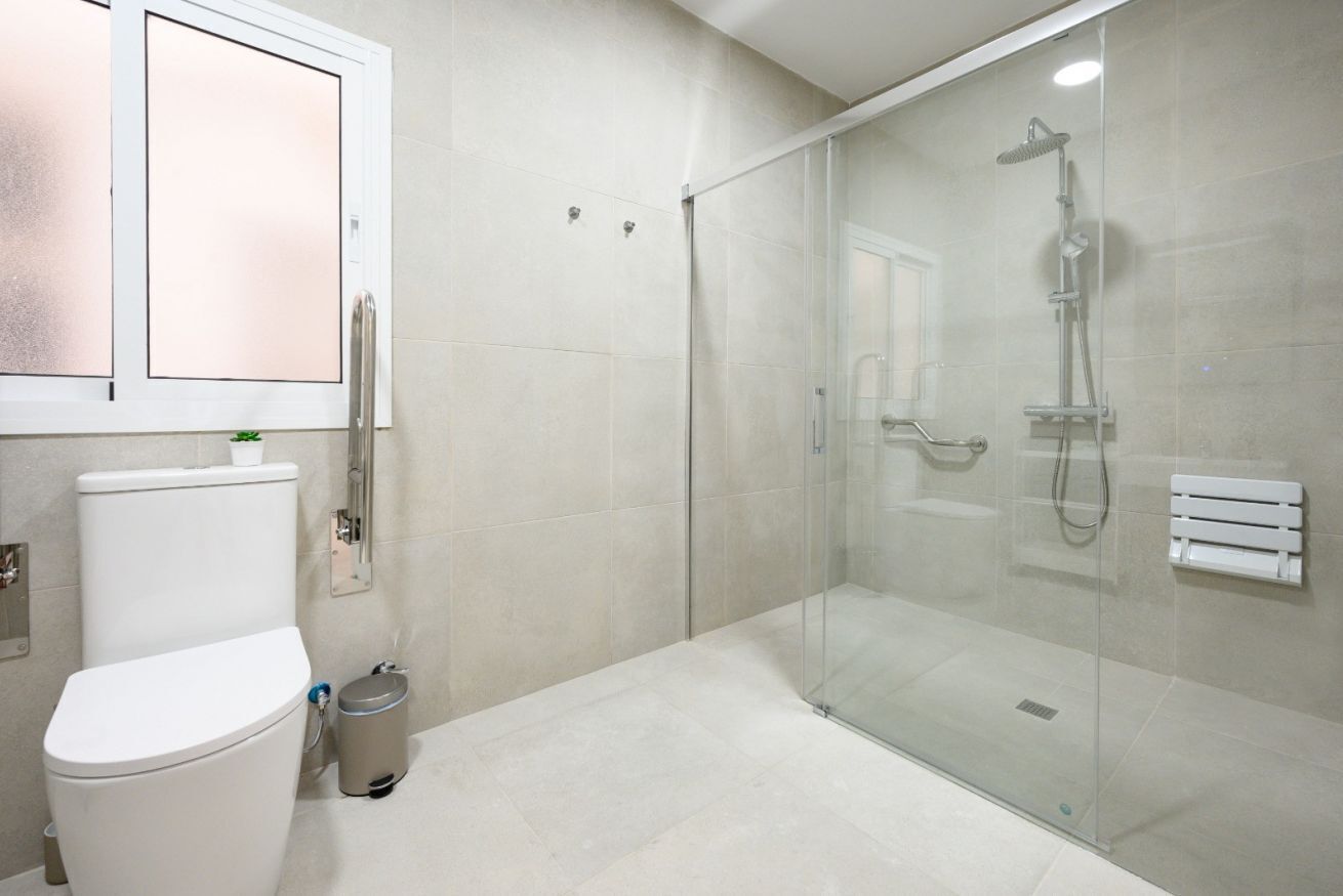 Een moderne badkamer met toilet, douchecabine en een vloer van witte tegels.