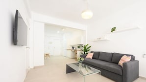 Una sala de estar moderna con un sofá gris, una mesa de centro de vidrio y un televisor de pantalla plana montado en la pared.