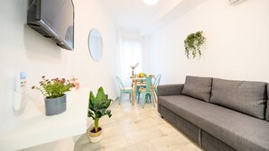 A modern living room with a grey sofa, a TV mounted on the wall, a small dining table with chairs, and a potted plant. - 2 min to the beach. Modern apartment (fuengirola)