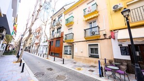 A street with buildings, a sidewalk, and a small outdoor seating area with tables and chairs. - 2 min to the beach. Modern apartment (fuengirola)
