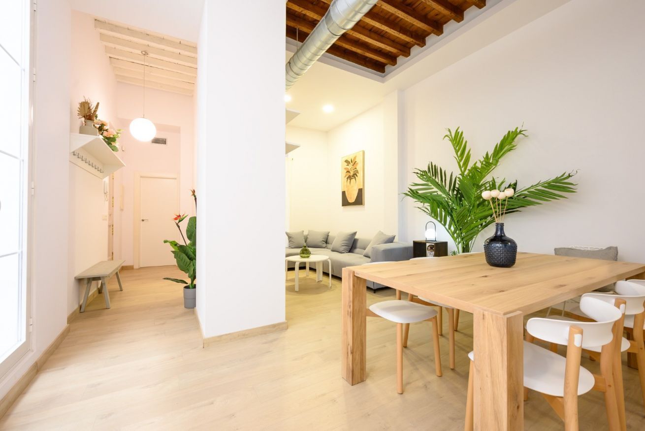 Een moderne woonruimte met een houten eettafel, witte stoelen, een bank en een grote kamerplant.