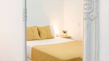 A neatly made bed with a yellow bedspread and pillows, a bedside table with a lamp and a small plant, and a decorative mirror with an ornate frame.