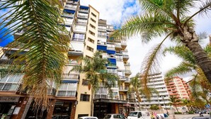 Un edificio de varios pisos con balcones, coches aparcados y palmeras.