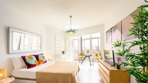 Un dormitorio moderno con cama, mesita de noche y escritorio con silla. Hay una ventana que proporciona luz natural y vistas a la ciudad.