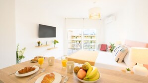 A breakfast setup with croissants, fruit, and juice on a wooden table, with a TV and balcony view in the background. - New Studio. Terrace & pool by 10ToSea (Fuengirola)