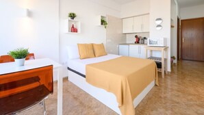 A modern bedroom with a bed, bedside table, and a small kitchen area with cabinets and a microwave. - Sea & Mountain views from a 10th floor studio with terrace by 10ToSea (Fuengirola)