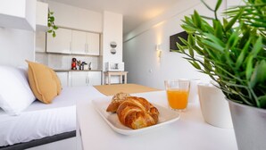 A modern hotel room with a bed, a breakfast table with croissants and orange juice, a potted plant, and a kitchenette in the background. - Sea & Mountain views from a 10th floor studio with terrace by 10ToSea (Fuengirola)