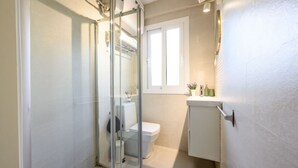 Ett modernt badrum med en duschkabin i glas, en vit toalett och ett litet handfat med plats för toalettartiklar.
