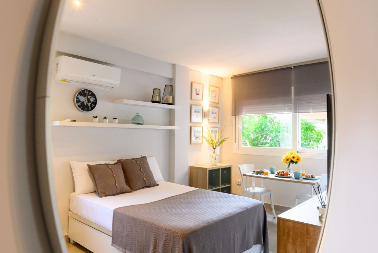 A modern bedroom with a bed, bedside table, and a window with a view of greenery.