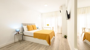 A modern bedroom with a bed, bedside tables, a small table with a lamp, and a mirror.