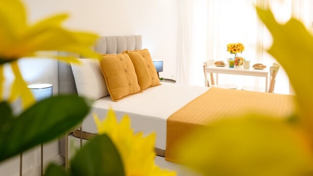 A hotel room with a bed, a bedside table, a chair, and a small table with a vase of flowers.