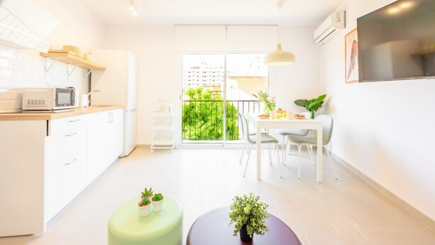 Une cuisine moderne et lumineuse, avec des meubles blancs, un four à micro-ondes et un coin repas comprenant une table et des chaises.