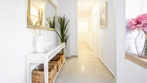 Un couloir avec une console blanche, des paniers en osier, un grand miroir et une plante en pot.