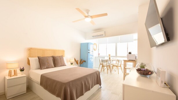 A bedroom with a bed, bedside table, lamp, and a desk with a bowl of flowers. - Nice studio at 3min to the beach new refurbished by 10ToSea (Fuengirola)