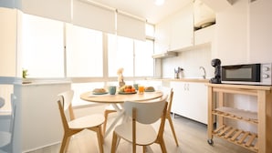 A modern kitchen with white cabinets, a round dining table with chairs, and a microwave on a wooden cart. - Nice studio at 3min to the beach new refurbished by 10ToSea (Fuengirola)