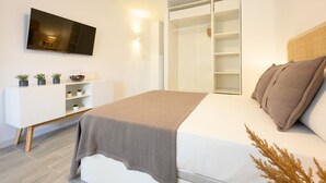 A modern bedroom with a bed, a TV mounted on the wall, a wardrobe, and a bedside table with plants. - Nice studio at 3min to the beach new refurbished by 10ToSea (Fuengirola)