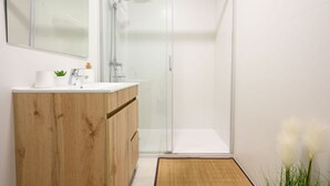 A modern bathroom with a glass shower enclosure, a wooden vanity, and a large mirror.