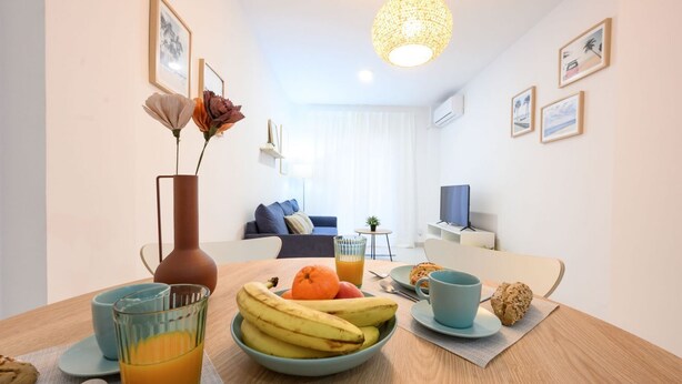 A dining area with a table set for breakfast, including a bowl of fruit, a glass of orange juice, and a cup.