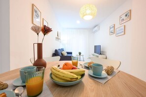 Un coin repas avec une table mise pour le petit-déjeuner, comprenant un bol de fruits, un verre de jus d’orange et une tasse.