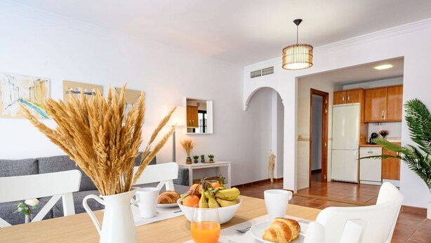 Ein modernes Wohnzimmer mit Esstisch, gedeckt für das Frühstück, einer Küche im Hintergrund und einem weißen Sofa.