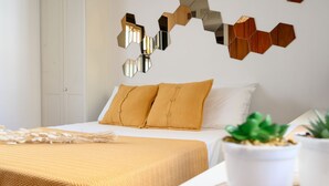 Ein Schlafzimmer mit einem Bett, zwei senfgelben Kissen, einem weißen Kopfteil und einem Wandspiegel mit sechseckigen Rahmen.