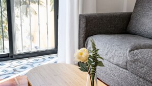 Ein Zimmer mit einem grauen Sofa, einem Holztisch und einer Vase mit einer weißen Blume.