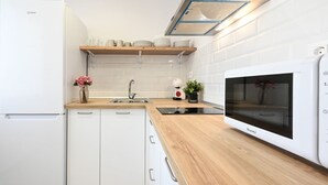A modern kitchen with white cabinetry, a wooden countertop, a built-in microwave, and a small shelf with dishes. - New 2 bedroom, city & beach by 10ToSea (Fuengirola)
