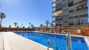 Una piscina con sillones de descanso y un edificio con balcones.