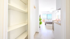 Un estrecho pasillo con paredes blancas y piso de baldosas que conduce a una habitación con cama, escritorio y ventana.