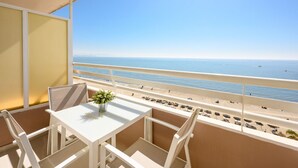 Un balcón con una mesa y sillas blancas, una planta en maceta y vistas a la playa y al océano.