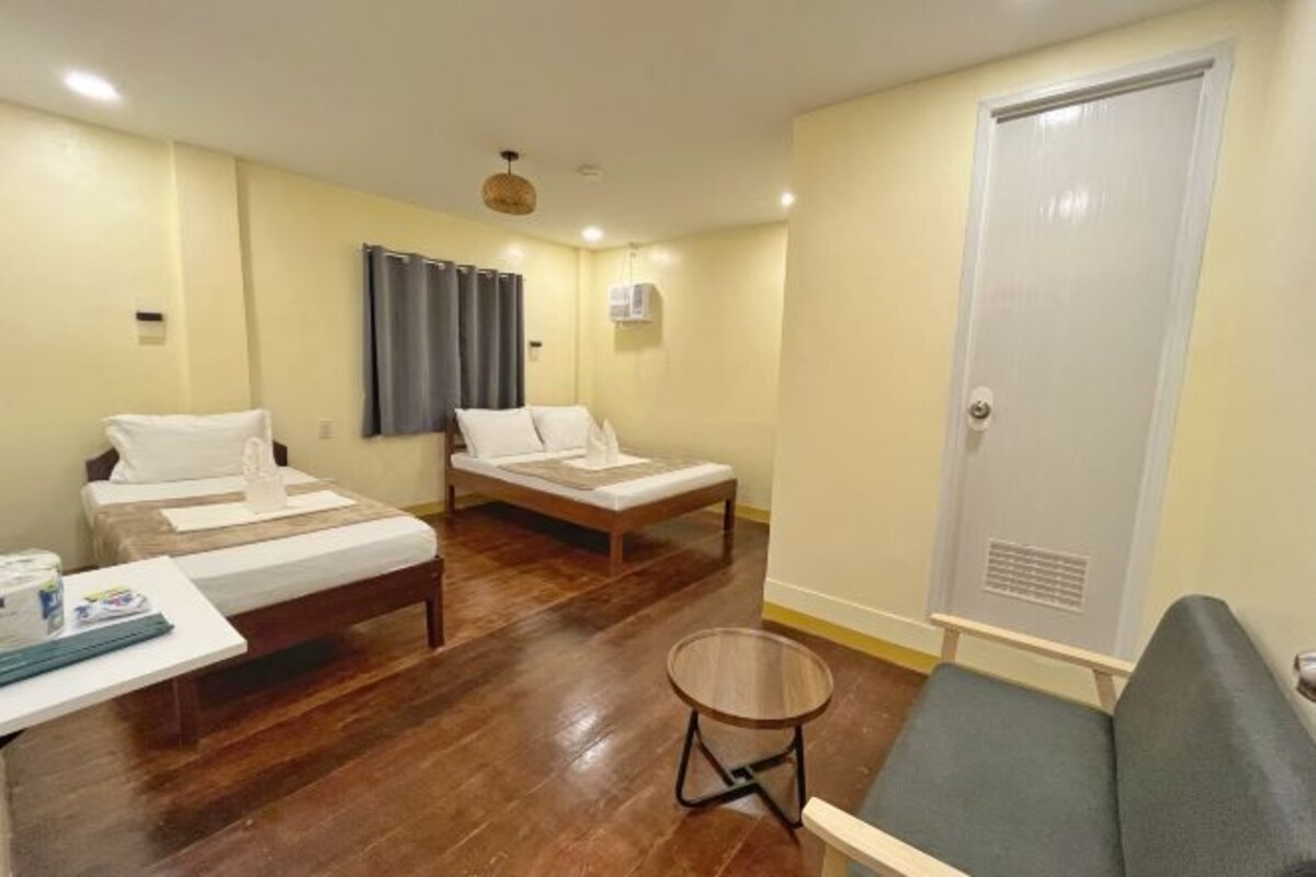 A hotel room with two single beds, a small round table, a sofa, a curtain, and a door.