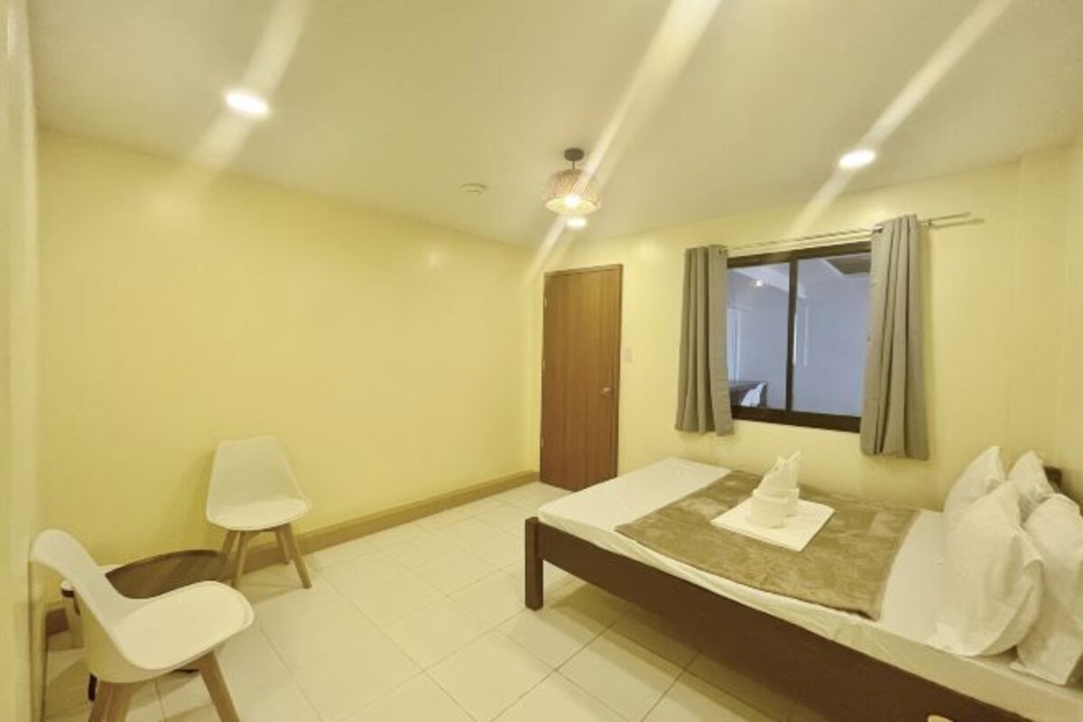 A bedroom with a bed, a chair, a window with curtains, and a door.
