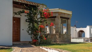 A building with a stone facade, a wooden door, and a garden with red flowers. - Beautiful Vista Blu Resort No2148 (Alghero)