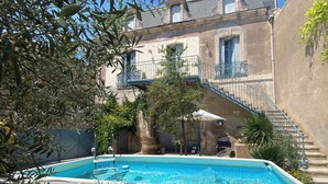 A swimming pool with a stone wall, a wooden barrel, and a staircase leading to a balcony. - Historical wine-growing house with lovely garden (Montagnac)
