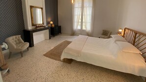 A bedroom with a large bed, a bedside table with a lamp, a chair, a dresser, and a window with curtains. - Historical wine-growing house with lovely garden (Montagnac)
