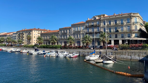 A waterfront with boats docked, a row of historic buildings, and a clear blue sky. - Historical wine-growing house with lovely garden (Montagnac)