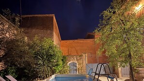 A swimming pool with a tiled deck, surrounded by plants and trees, with a building in the background. - Historical wine-growing house with lovely garden (Montagnac)