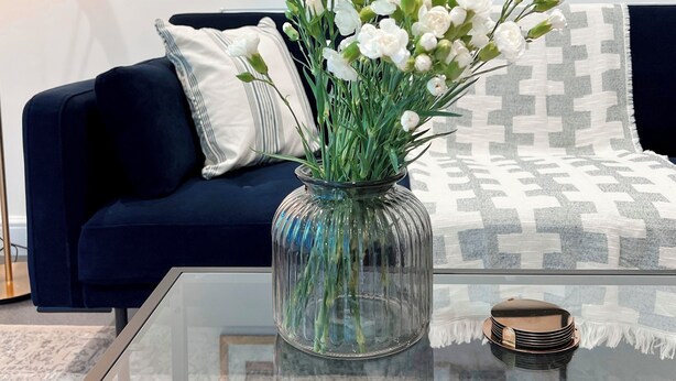 A living room with a dark blue sofa, a glass coffee table, a vase with white flowers, and framed artwork on the wall. - 4 Beds House Coventry Sleep 7 With 3parking Spaces (Coventry)