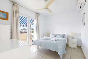 A bedroom with a bed, nightstands, a ceiling fan, and a view of the outside.