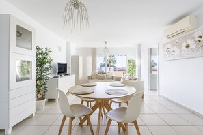 A modern dining area with a round table, chairs, a potted plant, and a television.