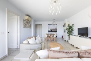 Uma sala moderna com sofá, mesa de centro, área de refeições, cozinha e televisão.