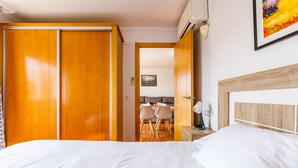 A hotel room with a large bed, wooden wardrobe, a dining area with chairs, and a painting on the wall.