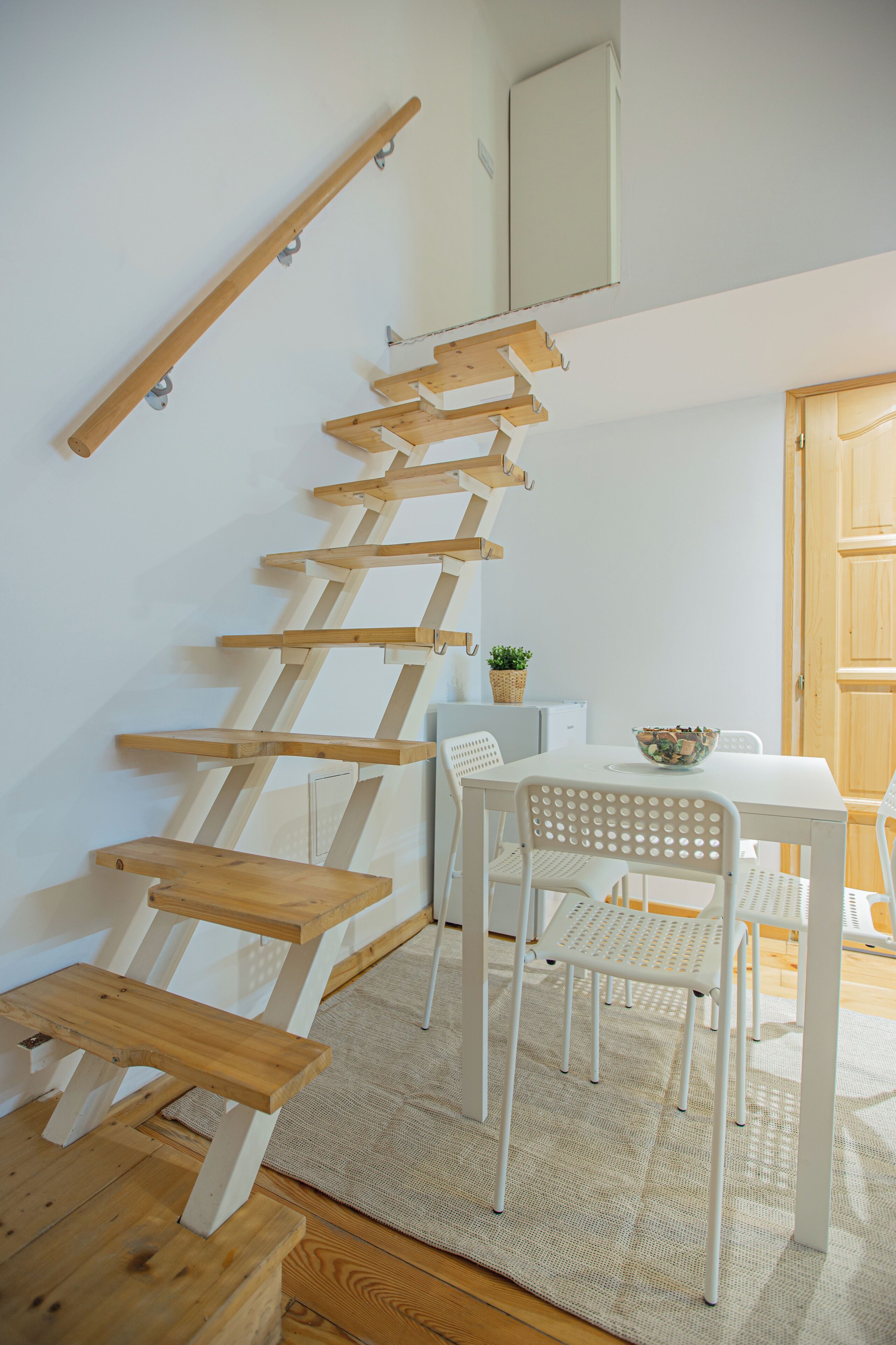 A staircase with wooden steps and a white wall. There is a white table with chairs and a bowl on it.